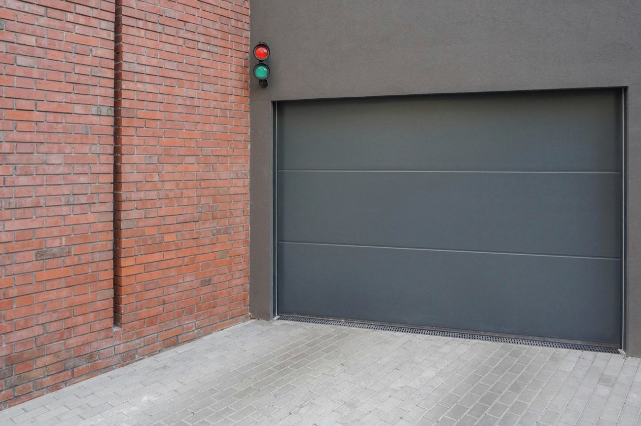 A grey sectional garage door beside a brick wall